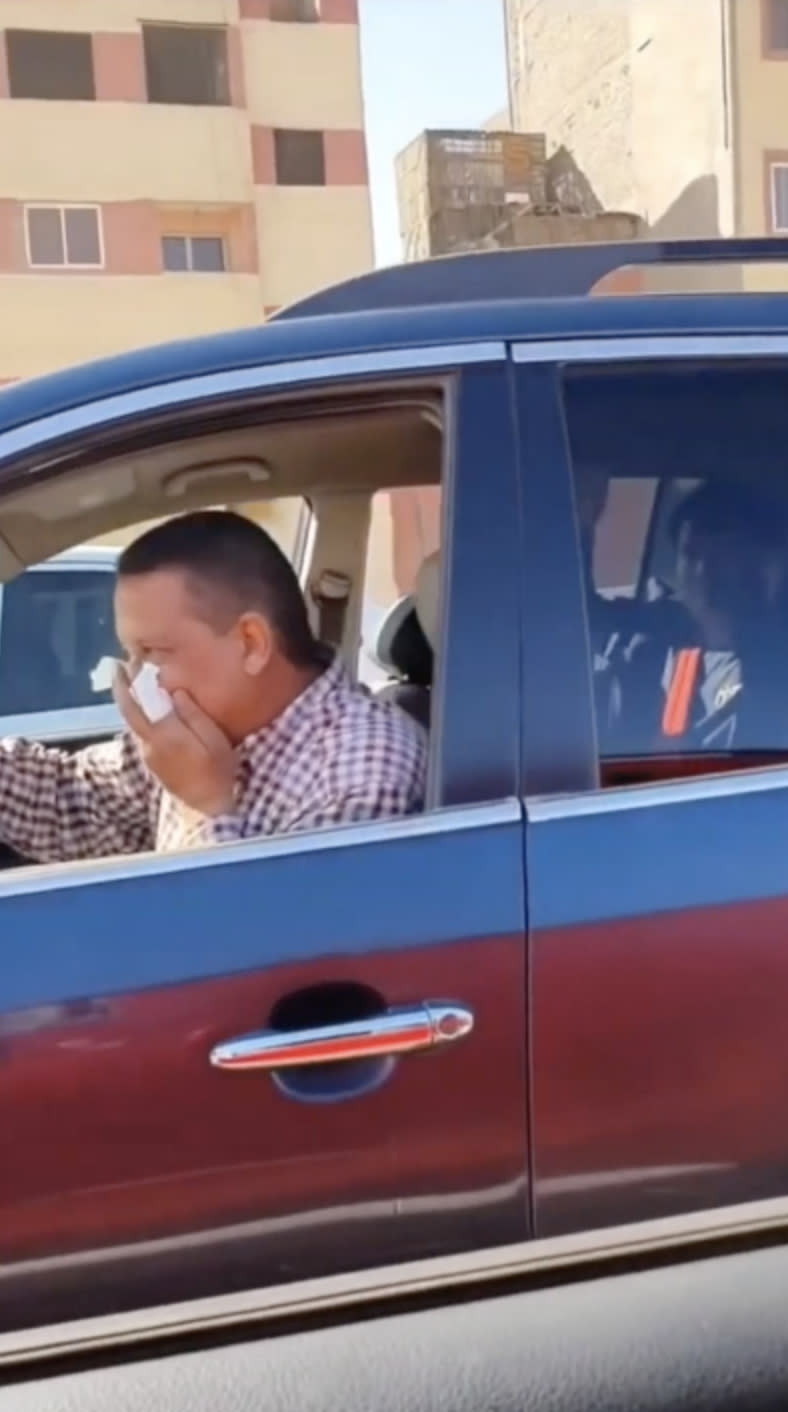 Pictured is a taxi driver covering his face with a tissue as his Chinese passenger sits in the back seat. 