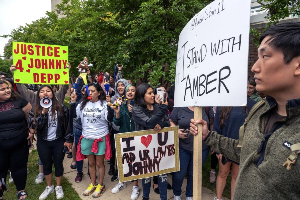 A crowd holds signs, some in support of Johnny Depp and one in support of Amber Heard