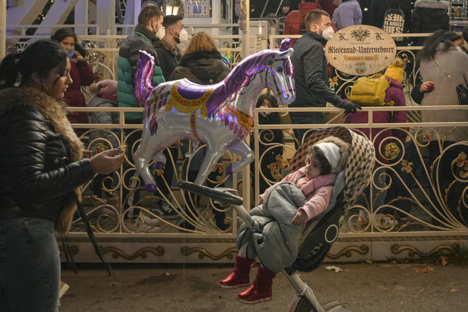 A child sits in a stroller as people wait to get on a carousel at a Christmas market in Vienna, Austria, Sunday, Nov. 21, 2021. The Austrian government announced a nationwide lockdown that will start Monday and comes as average daily deaths have tripled in recent weeks and hospitals in heavily hit states have warned that intensive care units are reaching capacity.(AP Photo/Vadim Ghirda)