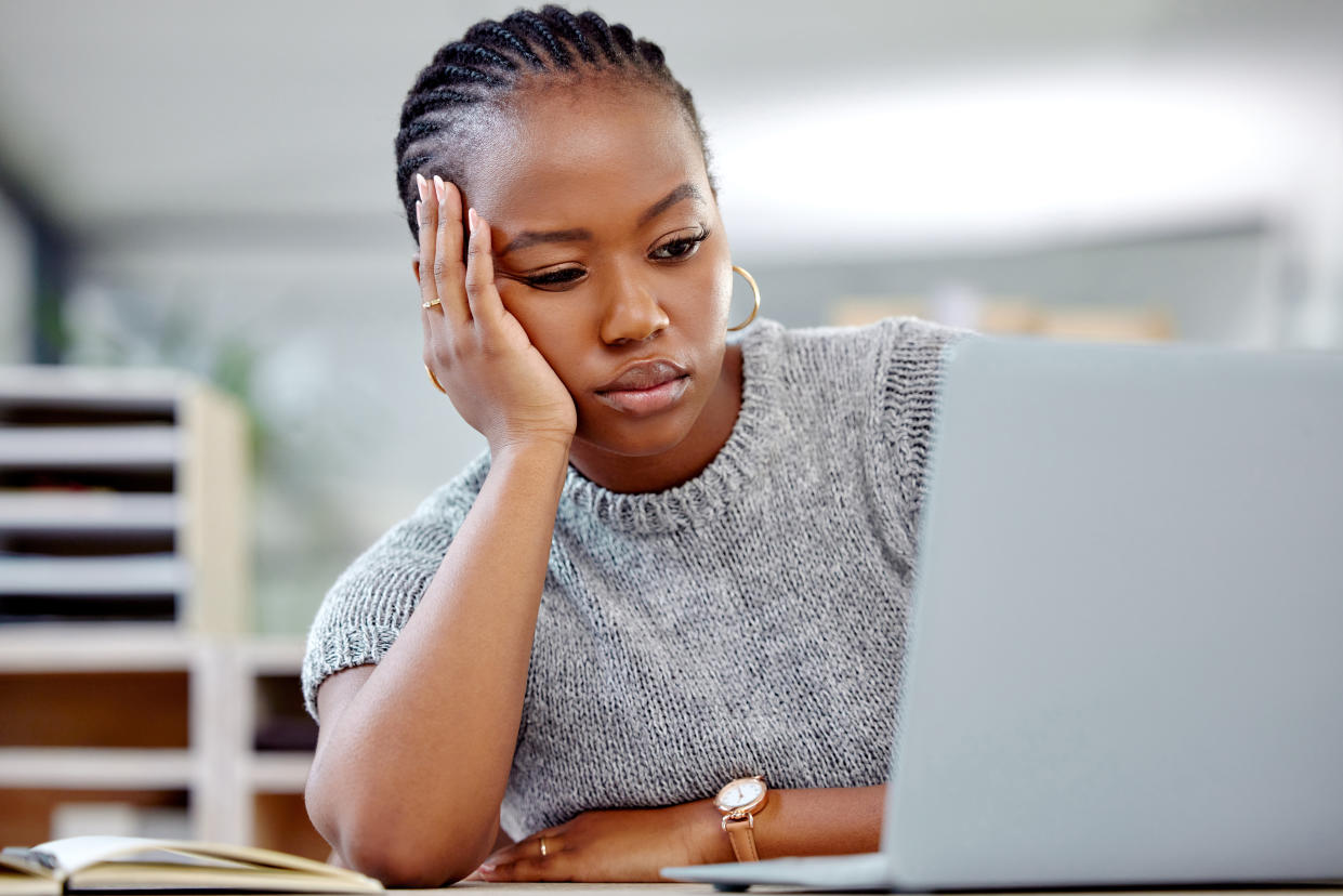 Pretty black woman with head on hand as she waits for her laptop to boot up.