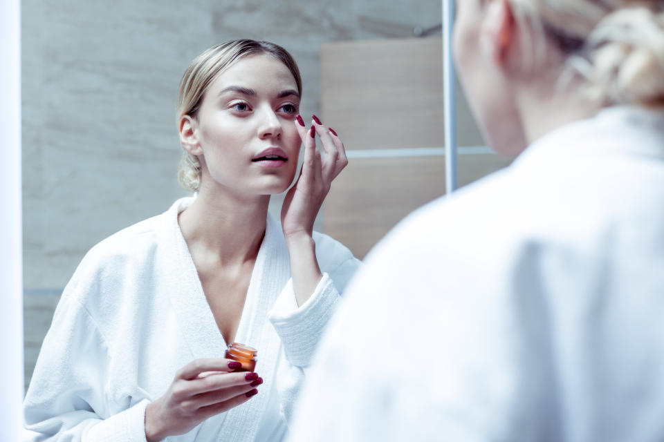 Cream under eyes. Blue-eyed beautiful appealing woman putting some nourishing cream under her eyes