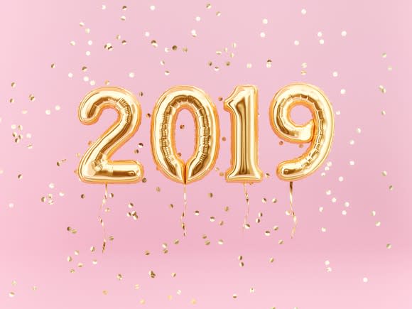 Gold balloons spelling out 2019 against pink background with gold confetti falling all around.
