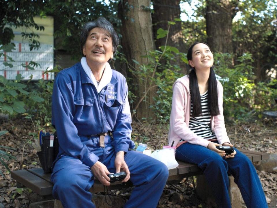 An older Japanese man and a teenage girl sit on a bench smiling.