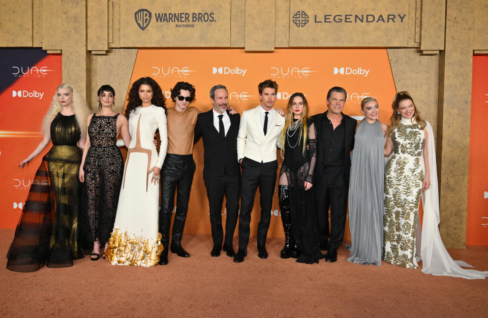 Cast of "Dune" posing at premiere, in formal attire, with logo backdrop