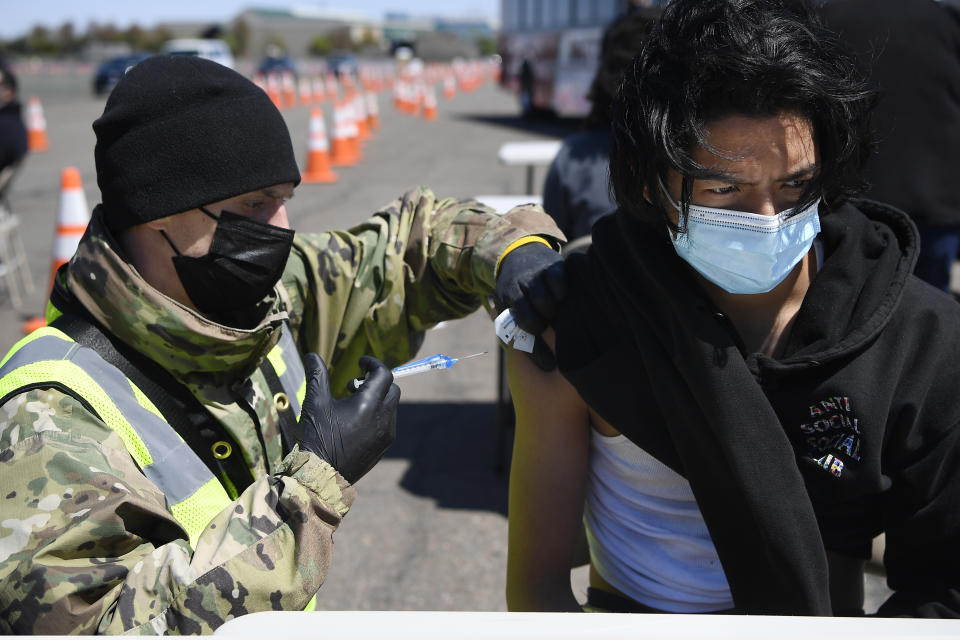 FILE - In this April 26, 2021, file photo Connecticut National Guard medic Todd Smith, left, administers a shot to East Hartford High School senior Alberto Salazar Rodriguez at a mass vaccination site at Pratt & Whitney Runway in East Hartford, Conn. Over the past year, National Guard members have been called in to battle the COVID-19 pandemic, natural disasters and race riots. (AP Photo/Jessica Hill, File)