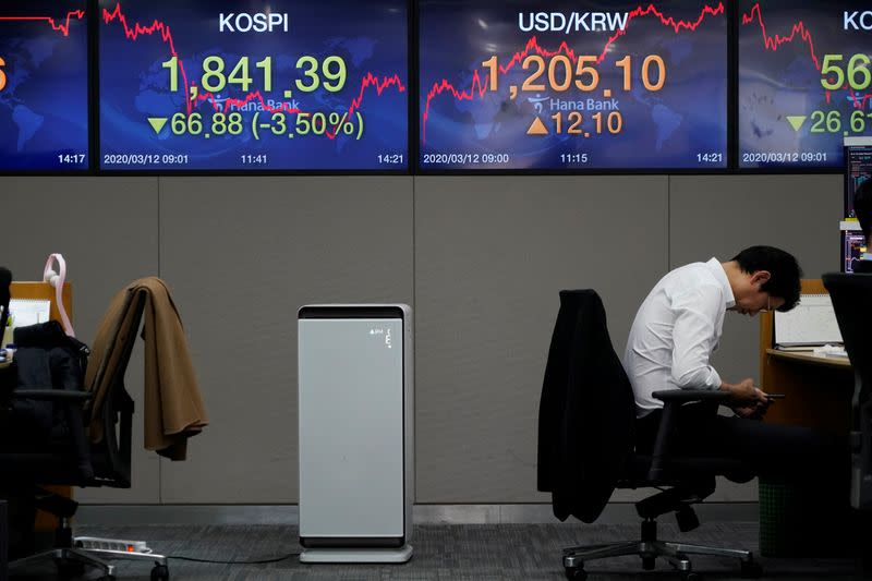 A currency dealer looks at his mobile phone in front of electronic boards showing the Korea Composite Stock Price Index (KOSPI) and the exchange rate between the U.S. dollar and South Korean won, at a dealing room of a bank in Seoul