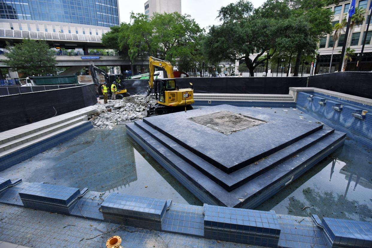 Crews continue the demolition of the water feature in downtown Jacksonville's James Weldon Johnson Park that contained the base and column of the confederate monument Monday. The remains of the monument were removed over the weekend and now construction fence obscures the two water features in the park and signs announce park renovations with a completion date as the summer of 2023.