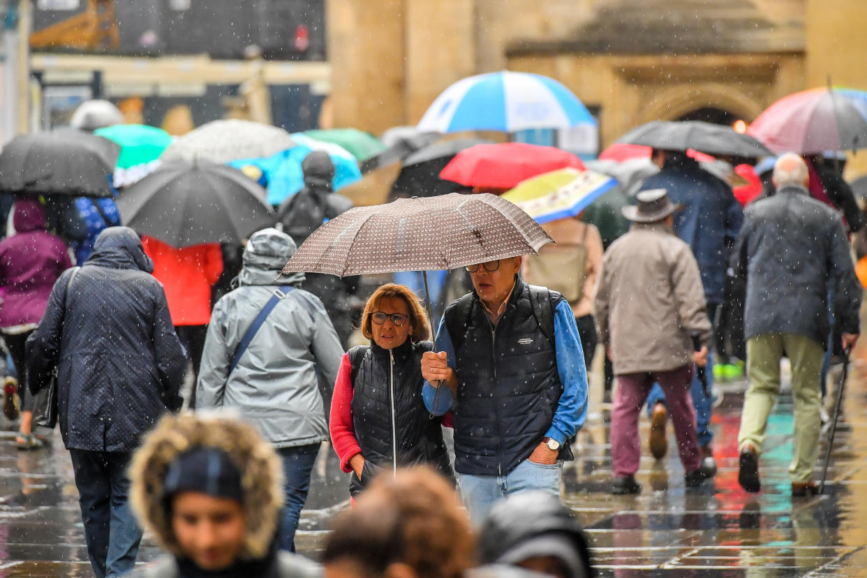 People use umbrellas as they cross Bath Abbey churchyard during a downpour in the centre of Bath (Picture: PA)