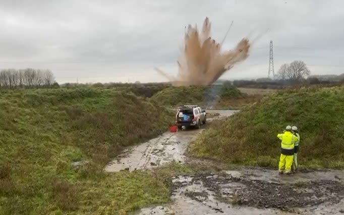 A minor explosion in a muddy field, two men in high-vis jackets look on from a distance