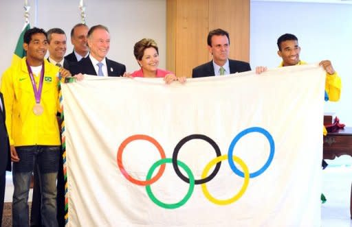 La bandera olímpica pasó fugazmente el martes por el despacho de la presidenta brasileña Dilma Rousseff, a manos del alcalde de Rio y los hermanos boxeadores Esquiva y Yamaguchi Falcao, al tiempo que el presidente del COI advirtió que Rio debe trabajar duro para los Juegos de 2016. (AFP | evaristo sa)