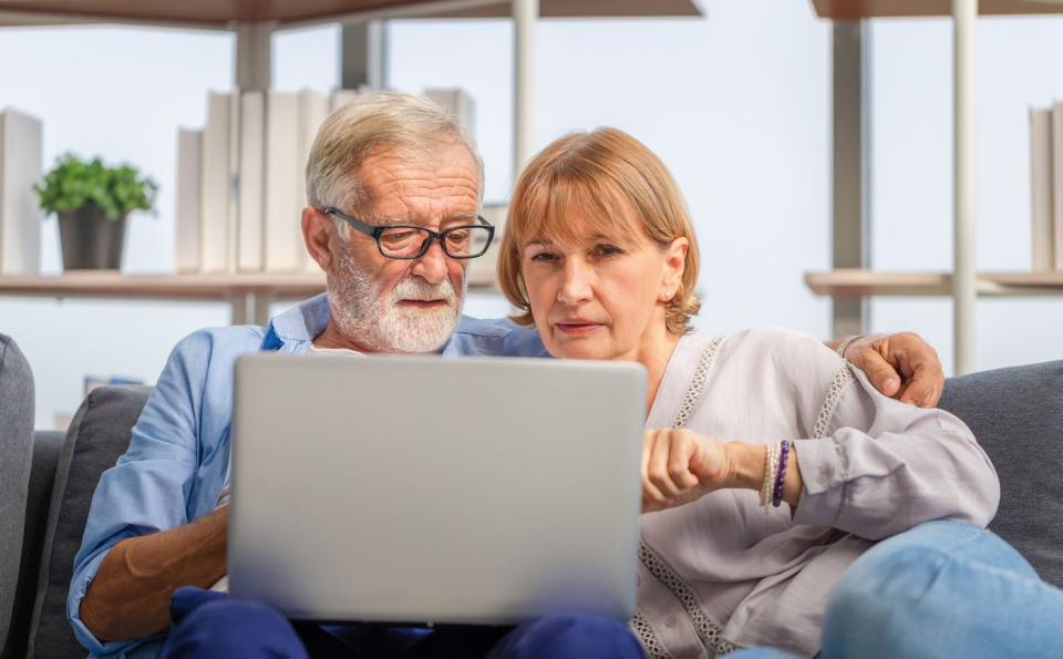 A couple sitting on a couch and looking at a laptop together.