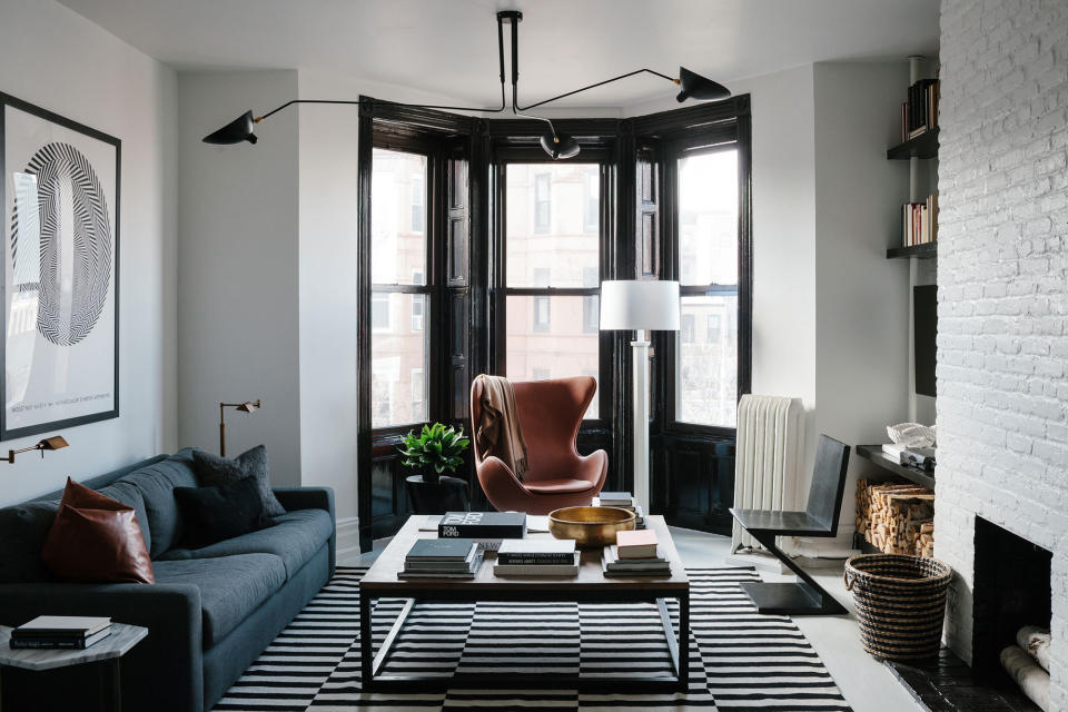 A living room with black glossy framed bay window, white walls, black and white rug and dark furniture