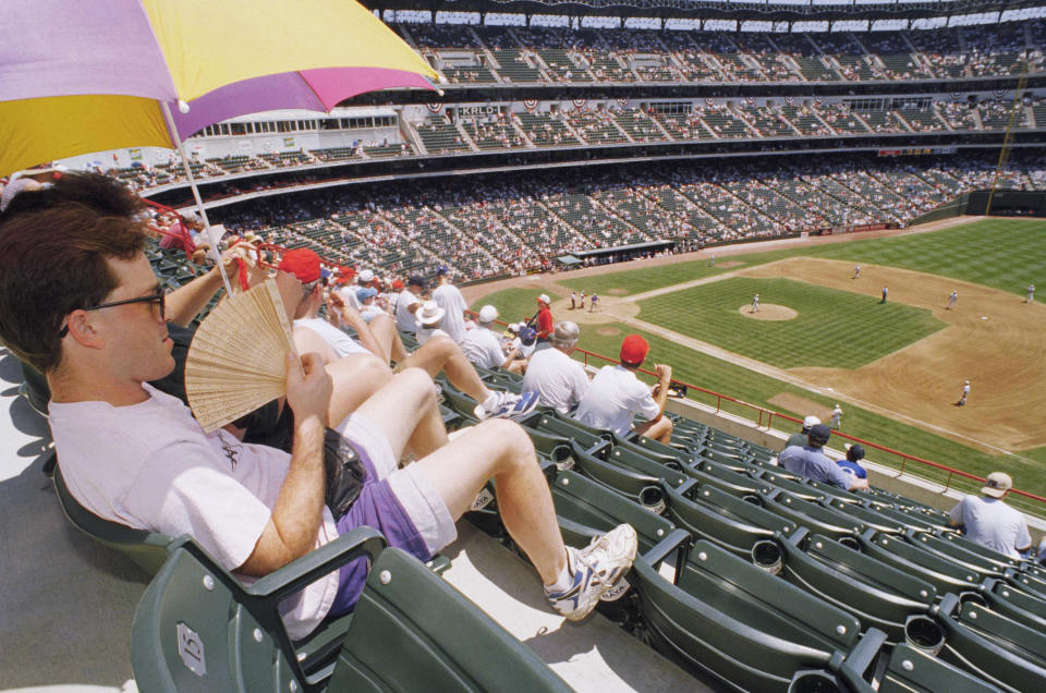 FILE - Scott Sarett, of Arlington, Texas, uses an umbrella and a fan to keep cool during the Legends of the Game at the Ballpark in Arlington during All-Star baseball festivities in Arlington, Texas, July 10, 1995. Major League Baseball is playing its All-Star Game in Arlington for the first time since 1995, when the Rangers played outside in the stifling heat. This year's game will be played Tuesday, July 16, 2024, in their stadium with a retractable roof that opened in 2020. (AP Photo/David J. Phillip, File)