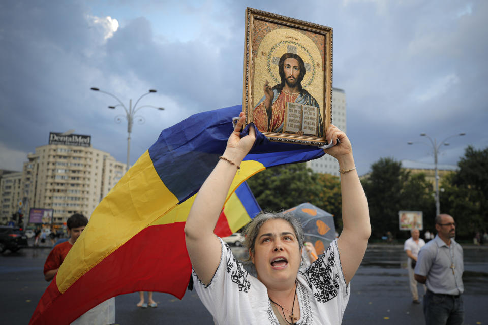 A woman shouts slogans holding a flag and a religious icon during a protest outside the government headquarters against recently passed legislation that enables authorities to impose quarantine or isolation measures on COVID-19 infected people in Bucharest, Romania,Sunday, July 19, 2020. Over the past week Romania has registered the highest number of COVID-19 infection cases since the pandemic reached the country in February, with up to 889 in a 24 hours interval, as many fail to observe the mandatory protection measures, like the use of a face mask indoors and on public transport or maintaining social distancing. (AP Photo/Vadim Ghirda)