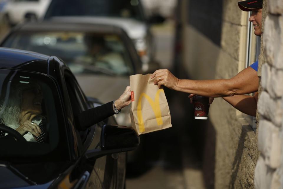 A McDonald's worker passes a woman a bag of food from the drive-thru window. 