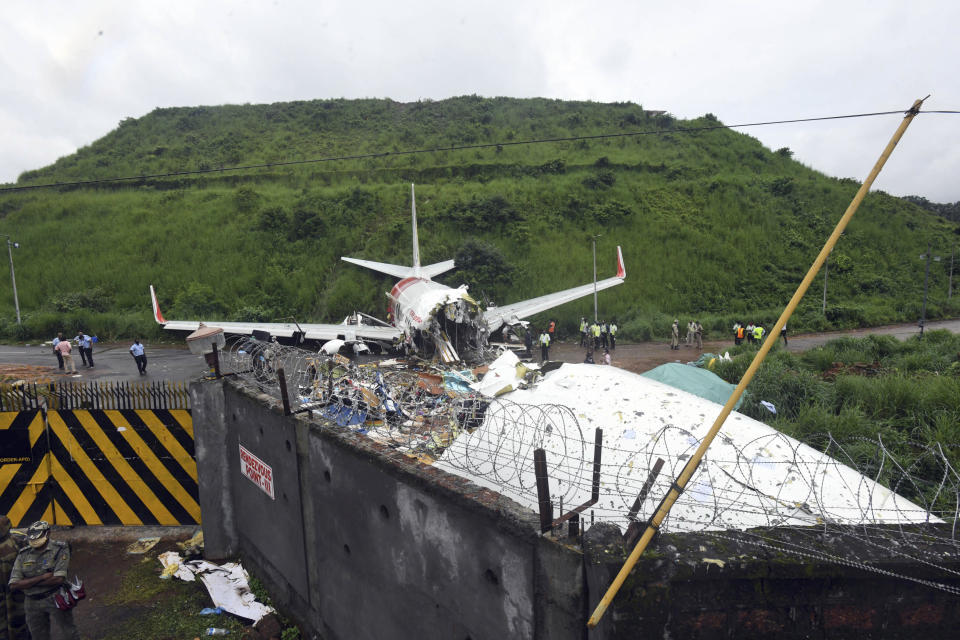 Officials stand by the debris of the Air India Express flight that skidded off a runway while landing in Kozhikode, Kerala state, India, Saturday, Aug. 8, 2020. The special evacuation flight bringing people home to India who had been trapped abroad because of the coronavirus skidded off the runway and split in two while landing in heavy rain killing more than a dozen people and injuring dozens more. (AP Photo/Shijith Sreedhar)