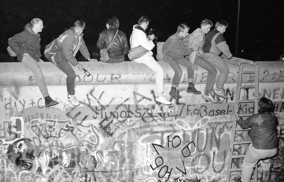 West German citizens sit on the top of the Berlin wall near the Allied checkpoint Charlie after the opening of the East German border was announced Nov. 9, 1989. (Photo: Fabrizio Bensch/Reuters)