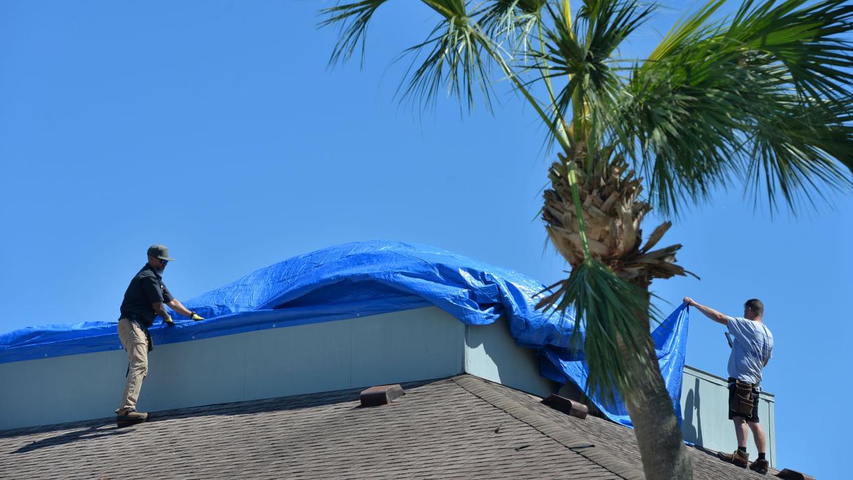 Workers use a blue tarp to cover the roof of a business in Punta Gorda, Florida, following Hurricane Ian on Friday, Sept. 30, 2022.