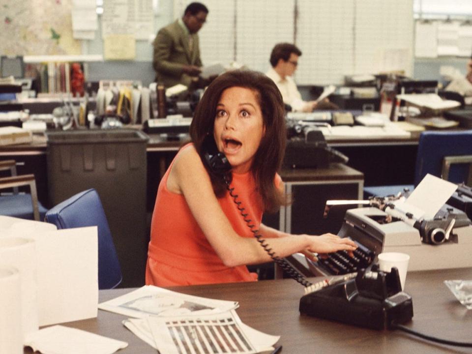 Mary on the phone and typing in an office with a surprised expression.