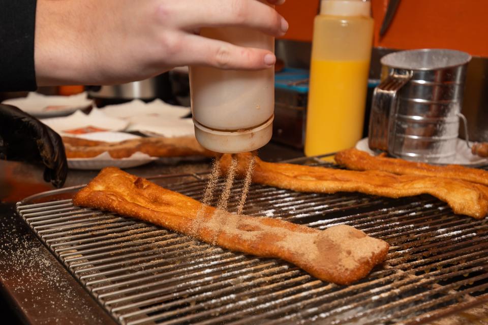 Employees shake a mixture of sugar and cinnamon over a freshly cooked fried dough. Blink's Fry Doe is celebrating its 50th year of operation at Hampton Beach in 2024.