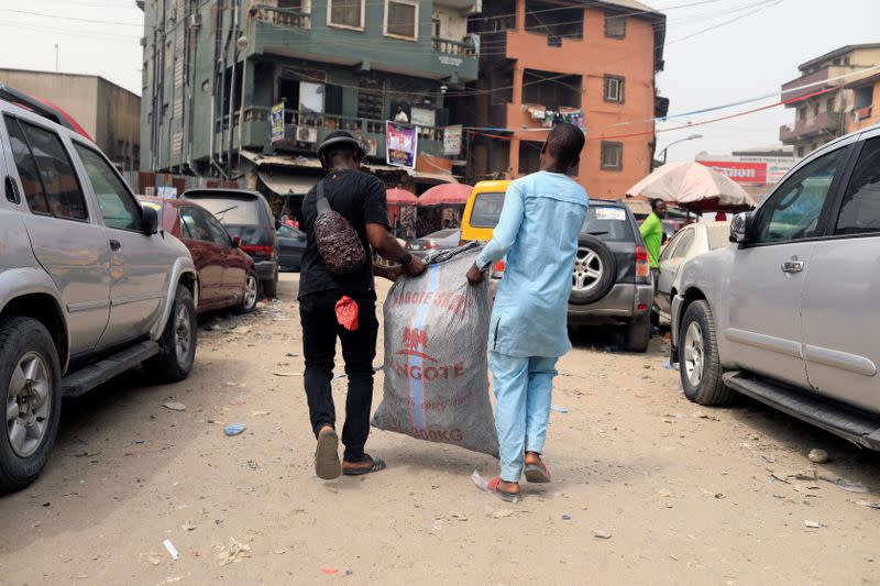 Visual artist Adeyemi Emmanuel (L) carries a sack filled with pieces of wooden frames he collected from a frame shop at Aroloya market in Lagos, Nigeria