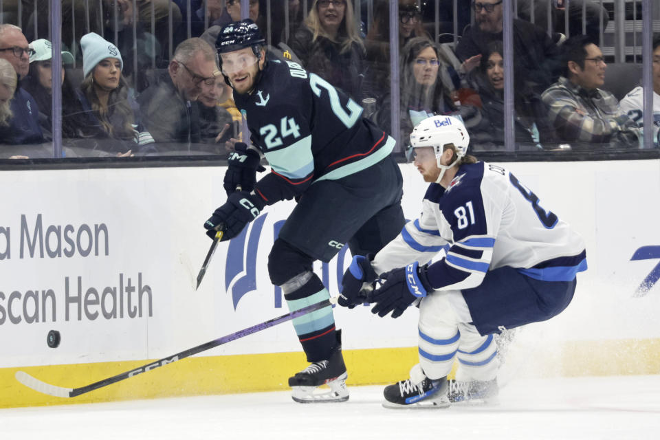 Seattle Kraken defenseman Jamie Oleksiak (24) and Winnipeg Jets left wing Kyle Connor (81) vie for the puck during the first period of an NHL hockey game, Friday, March 8, 2024, in Seattle. (AP Photo/John Froschauer)