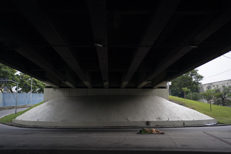 Una persona sin hogar duerme abajo de un autopista cerca del Sambódromo, que se está equipando para recibir a estar personas en medio de la epidemia del coronavirus en Río de Janeiro, Brasil, el lunes 30 de marzo de 2020. (AP Foto/Leo Correa)