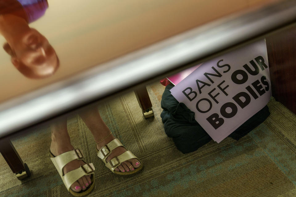 Planned Parenthood advocacy programs manager, Allison Terracio, is reflected in a table as signs sit in the clinic's office in Columbia, S.C., Friday, May 27, 2022. Under South Carolina law, a woman arriving for an abortion would have already undergone a waiting period and been pointed toward a lengthy document detailing fetal development. Terracio, says those due in to take an abortion pill or undergo a brief surgery have already thought through what they wanted and nothing protesters can offer will change the circumstances of the prospective mother's life. "I'm not in the business of convincing anybody of anything," Terracio says. (AP Photo/David Goldman)