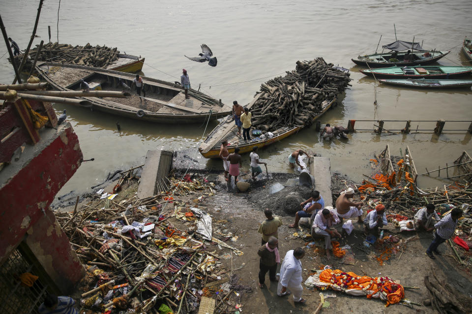 People wait for their turn to cremate a body as piles of logs arrive on boats at Manikarnika Ghat, one of the oldest and most sacred place for Hindus to be cremated, on the banks of river Ganges in Varanasi, India, Friday, Oct. 18, 2019. For millions of Hindus, Varanasi is a place of pilgrimage and anyone who dies in the city or is cremated on its ghats is believed to attain salvation and freed from the cycle of birth and death. Tens of thousands of corpses are cremated in the city each year, leaving half-burnt flesh, dead bodies and ash floating in the Ganges. (AP Photo/Altaf Qadri)