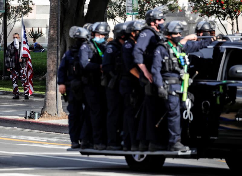 A supporter of U.S. President Donald Trump holds a U.S. flag as police officers in riot gear arrive at a rally in Los Angeles, California