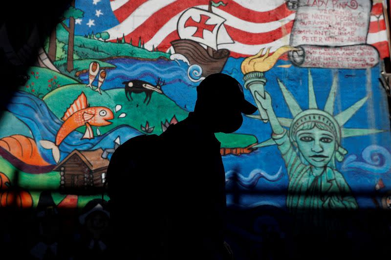 FILE PHOTO: A man in silhouette wearing a protective face mask walks past a mural, amid the coronavirus disease (COVID-19) pandemic, in the Queens borough of New York