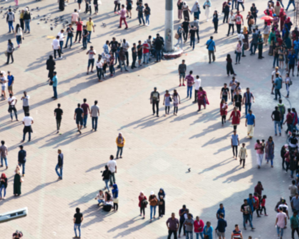 Blurred photo with daily life of city square - people crowd, spend their leisure hours, interact with each other.