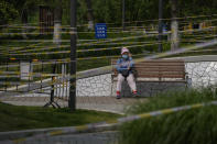 A woman wearing a face mask rests on a bench at the green space barricaded with fences and tapes to prevent residents from gathering due to pandemic measures on Thursday, May 19, 2022, in Beijing. (AP Photo/Andy Wong)