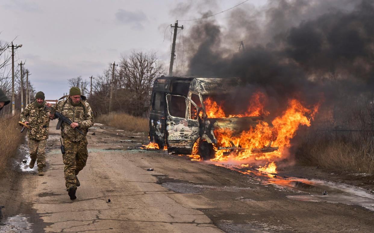 Ukrainian soldiers pass a bus burning after a Russian drone hit it near Bakhmut, in the Donetsk region