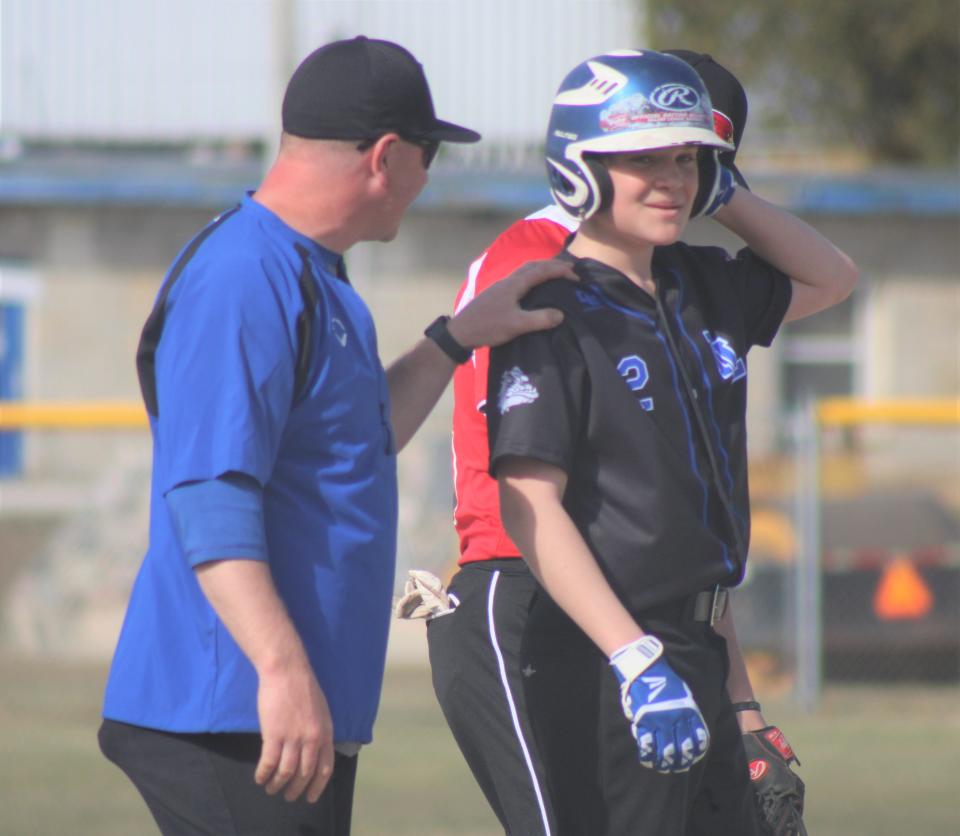 Inland Lakes freshman Ty Kolly (2) gets a pat on the shoulder from head coach Josh Vieau after getting over to third base in game one on Tuesday. Kolly delivered a hit for the Bulldogs earlier in the inning.