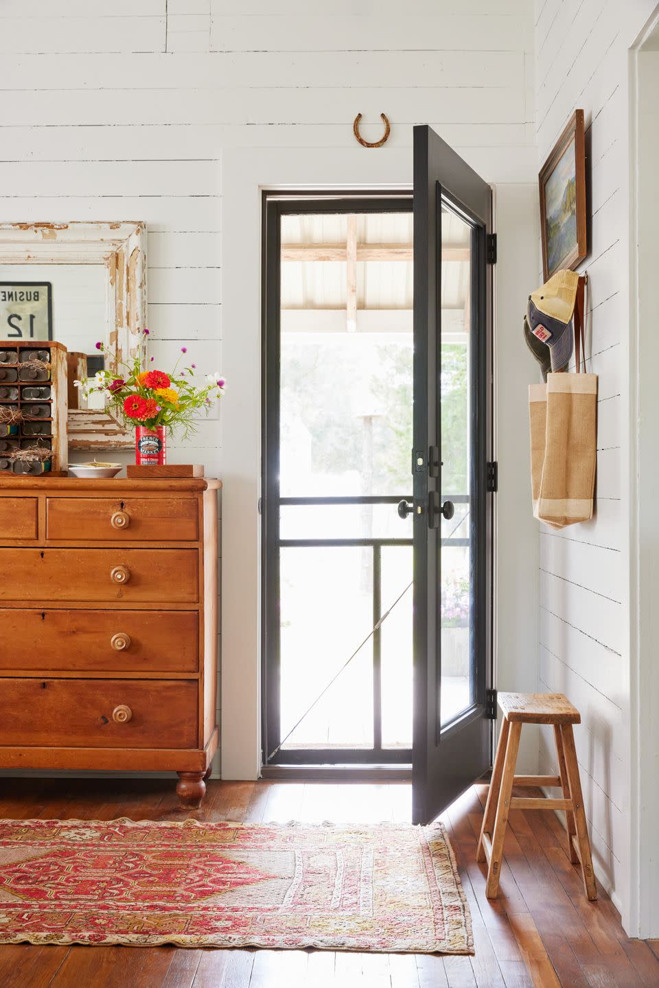 white entryway with screen door, pine dresser for storage stacked with antique decor