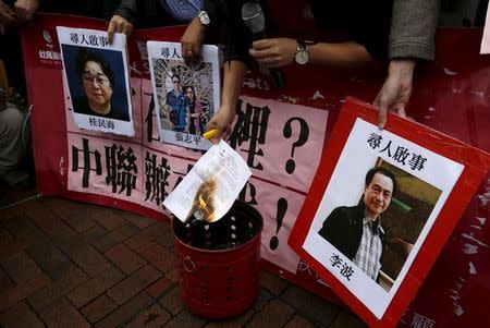 A pro-democracy demonstrator burns a letter next to pictures of missing staff members of a publishing house and a bookstore, including Gui Minhai, a China-born Swedish national who is the owner of Mighty Current, Cheung Jiping, the business manager of the publishing house and Causeway Bay Books shareholder Lee Bo (L-R), during a protest to call for an investigation behind their disappearance, outside the Chinese liaison office in Hong Kong, China January 3, 2016. REUTERS/Tyrone Siu
