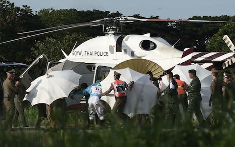 Rescue workers use umbrellas to a stretcher close to a police helicopter at a military airport in Chiang Rai  - Credit: LILLIAN SUWANRUMPHA /AFP/Getty