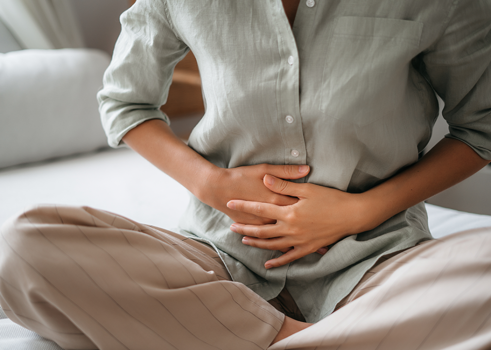 Person holding their hands against their stomach as they are seated on the ground.