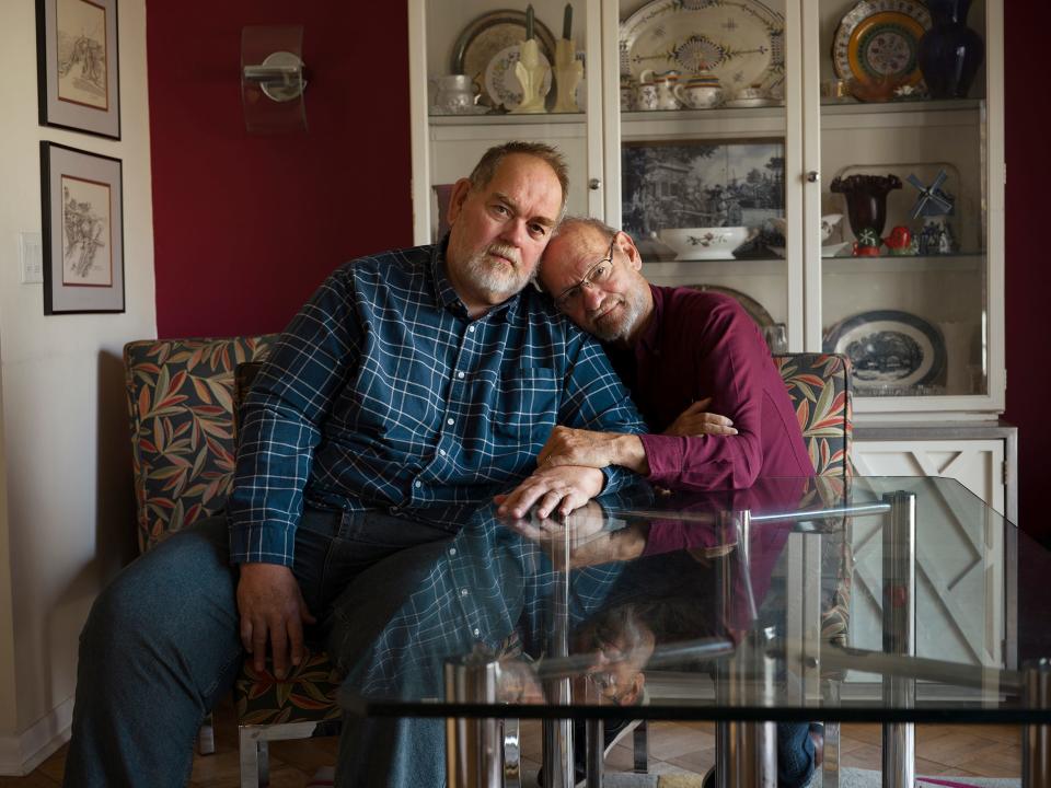 Older gay couple embracing and sitting on the couch facing the camera