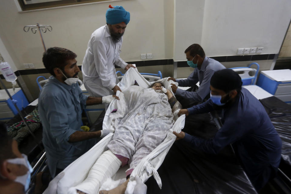 People shifts a woman, who was injured in bus and train accident, into bed after receiving initial treatment at a hospital in Sheikhupura near Lahore, Pakistan, Friday, July 3, 2020. A passenger train crashed into a bus carrying Sikh pilgrims at an unmanned railway crossing in eastern Pakistan, police and rescue officials said. (AP Photo/K.M. Chaudary)