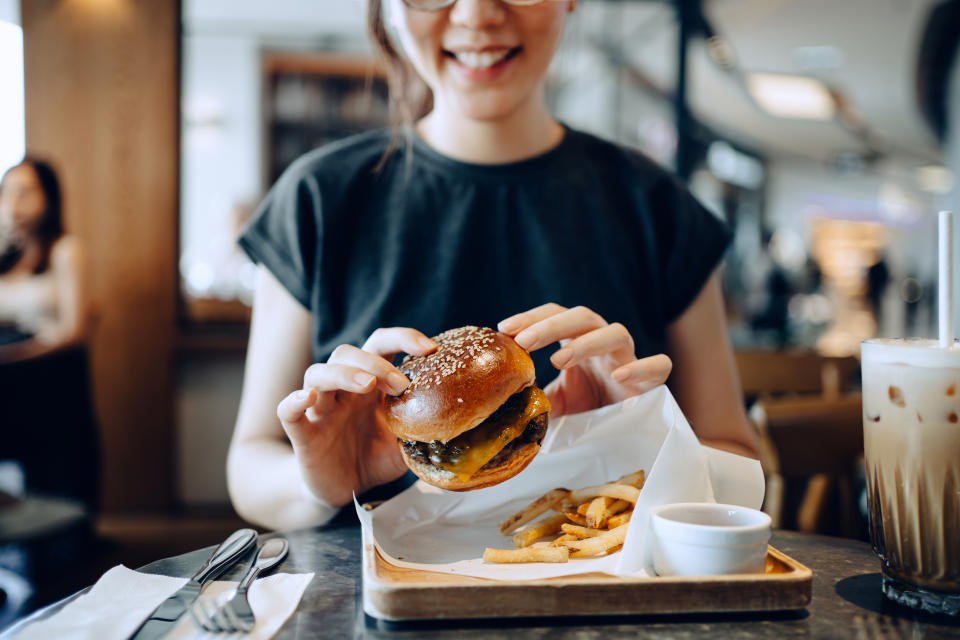 woman eating delicious burger with fries and a glass of iced coffee in a cafe