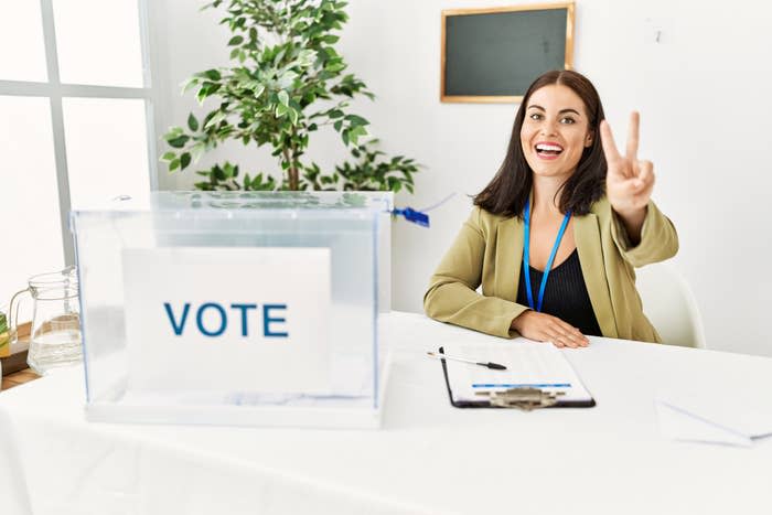 woman holding up a peace sign in front of a voting booth