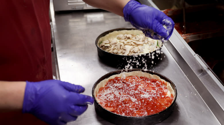 worker sprinkling cheese on pizzas 