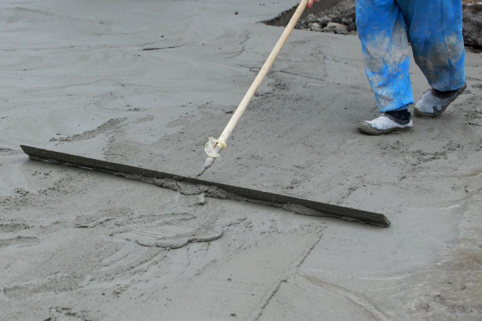 A close up of a worker in blue pants using a tool to level concrete.