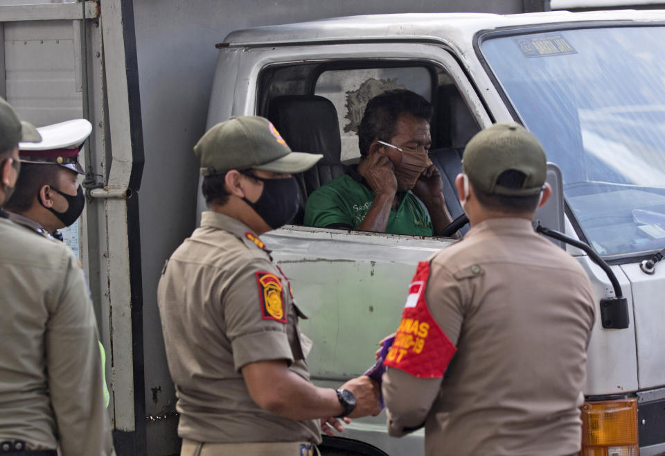 A truck driver puts on a mask given to him by Public Order Agency officers at a check point set up to enforce a city regulation requiring people to wear face masks in public places as a precaution against the coronavirus outbreak, in Medan, North Sumatra, Indonesia, Tuesday, Sept. 15, 2020. (AP Photo/Binsar Bakkara)