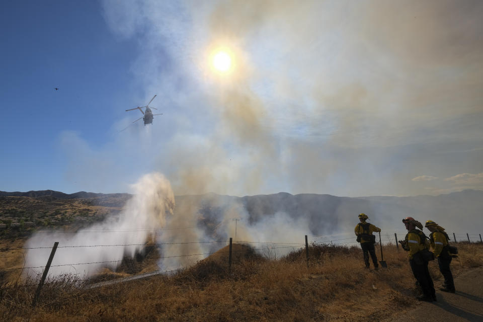 Firefighter watch as a helicopter drops water at a wildfire in Castaic, Calif., on Wednesday, Aug. 31, 2022. (AP Photo/Ringo H.W. Chiu)