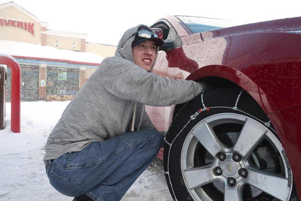 Taylor Killian puts snow chains on the vehicle he's driving during a trip to Flagstaff, Arizona, on Thursday, Feb. 21, 2019. Schools across northern Arizona canceled classes and some government offices decided to close amid a winter storm that's expected to dump heavy snow in the region. (AP Photo/Felicia Fonseca)