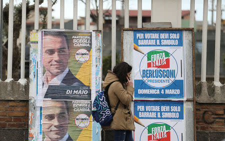 A woman walks past electoral posters of the 5 Star's candidate Luigi Di Maio and the Forza Italia party in Pomigliano D'Arco, near Naples, Italy, February 21, 2018. Picture taken February 21, 2018. REUTERS/Alessandro Bianchi