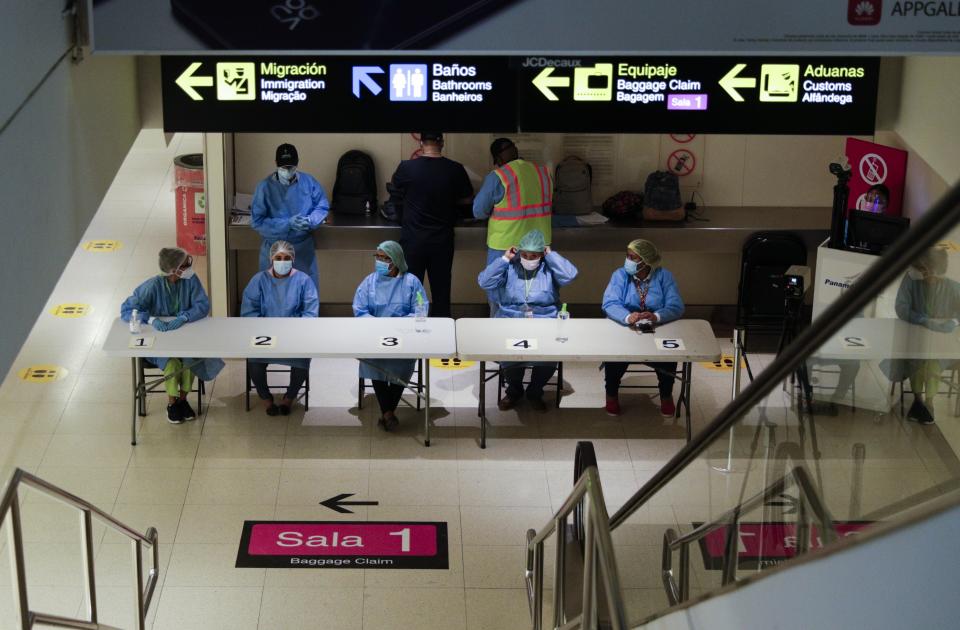 Health workers wait to revise arriving passengers' COVID-19 test results and administer tests to those who do not have one to show at Tocumen International Airport in Panama City, Monday, Oct. 12, 2020. Panama is lifting a broad spectrum of COVID-19 pandemic-related restrictions on Monday, including re-opening international flights and allowing hotels, casinos, and tourism-related activities. (AP Photo/Arnulfo Franco)